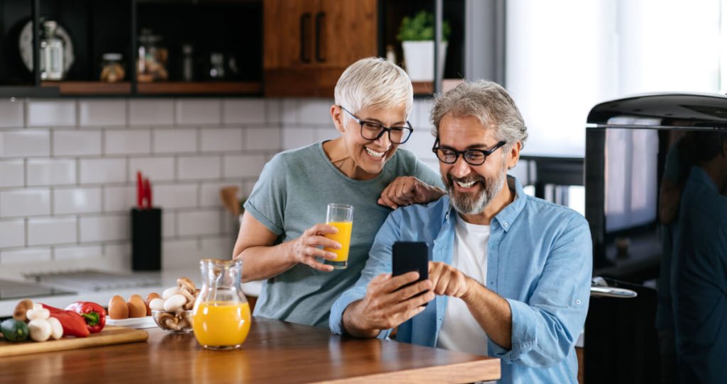 A happy couple using a phone together in the kitchen