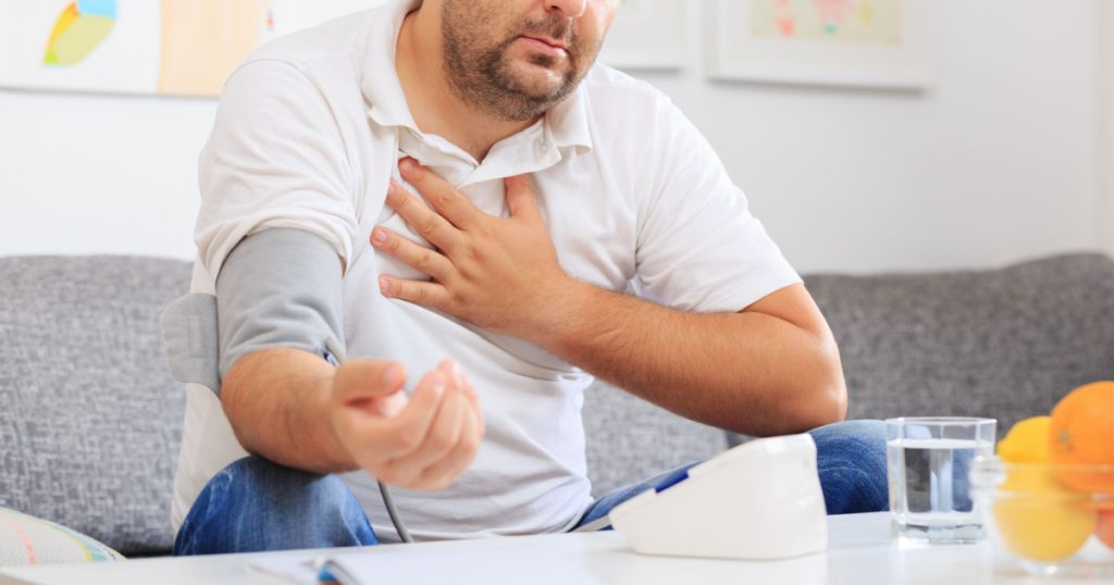 Man measuring his blood pressure and holding onto his chest