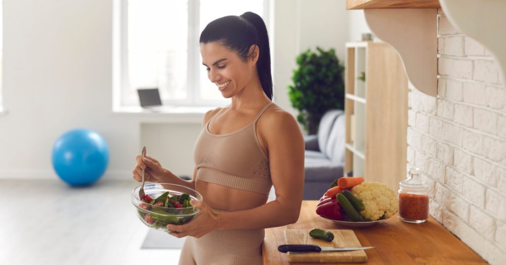 A happy looking woman eating a salad in the kitchen